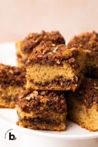 Squares of applesauce coffee cake with thick streusel topping, stacked on a cake platter.
