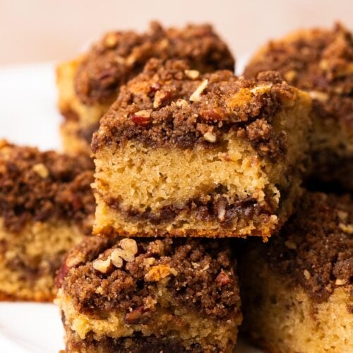 Squares of applesauce coffee cake with thick streusel topping, stacked on a cake platter.