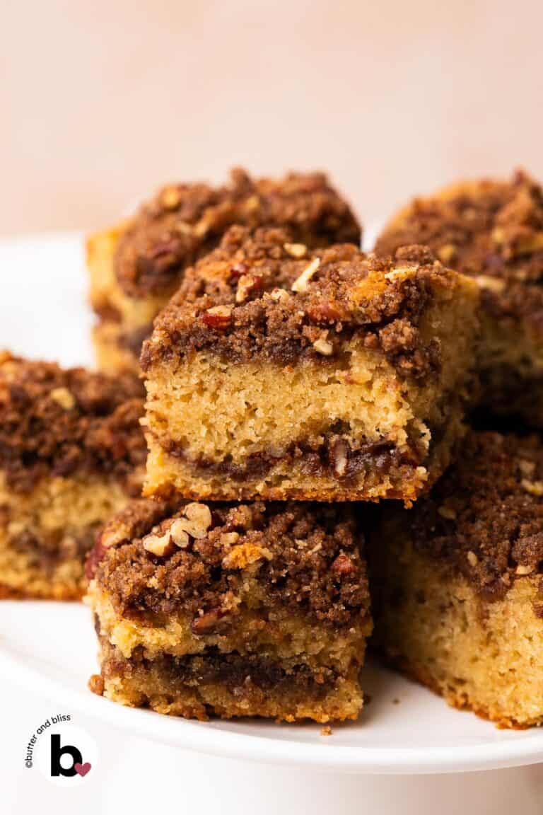 Squares of applesauce coffee cake with thick streusel topping, stacked on a cake platter.