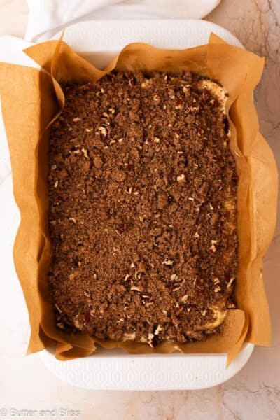Pecan streusel added to the top of coffee cake batter in a large baking dish.
