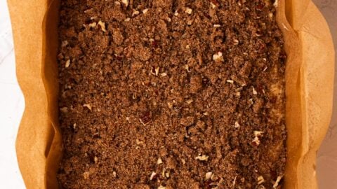 Pecan streusel added to the top of coffee cake batter in a large baking dish.