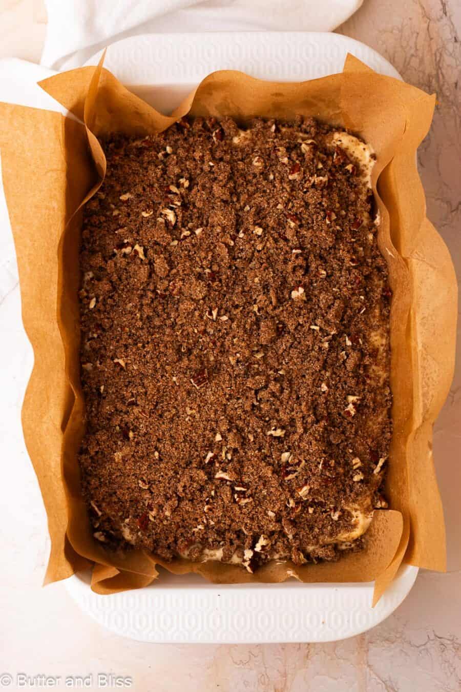Pecan streusel added to the top of coffee cake batter in a large baking dish.