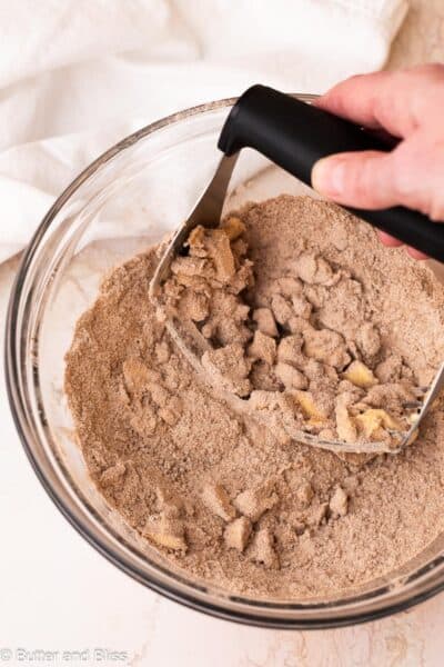 Butter being cut into cinnamon streusel in a mixing bowl with a pastry cutter.