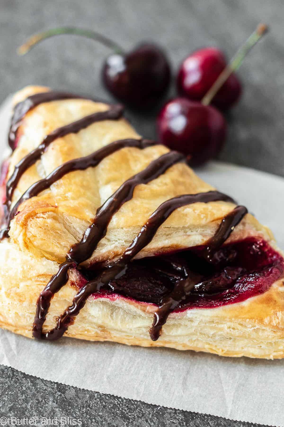 Cherry puff pastry turnover with chocolate drizzle on a napkin