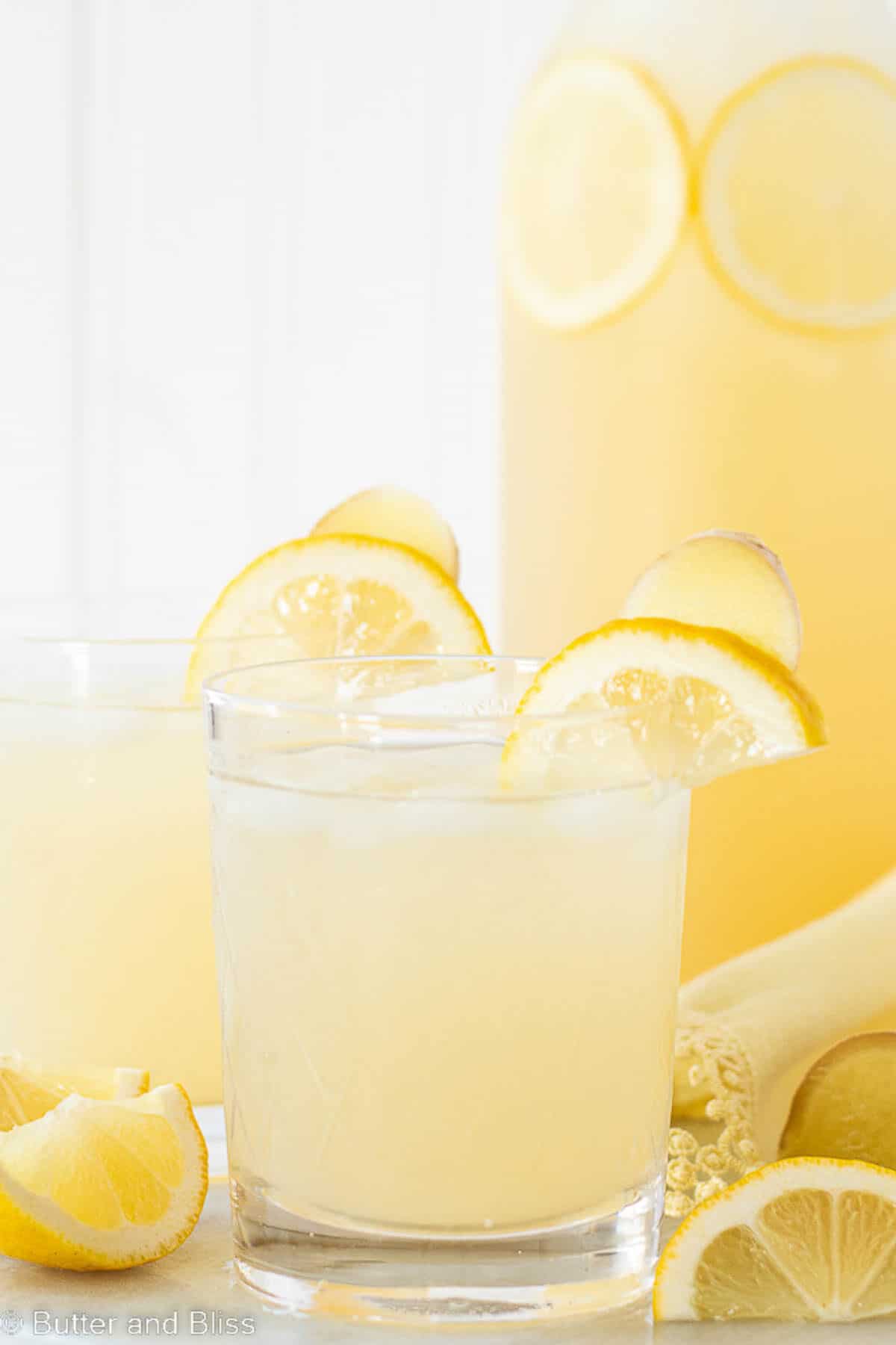 Ginger lemonade in glasses with lemon wedge on a table with a pitcher