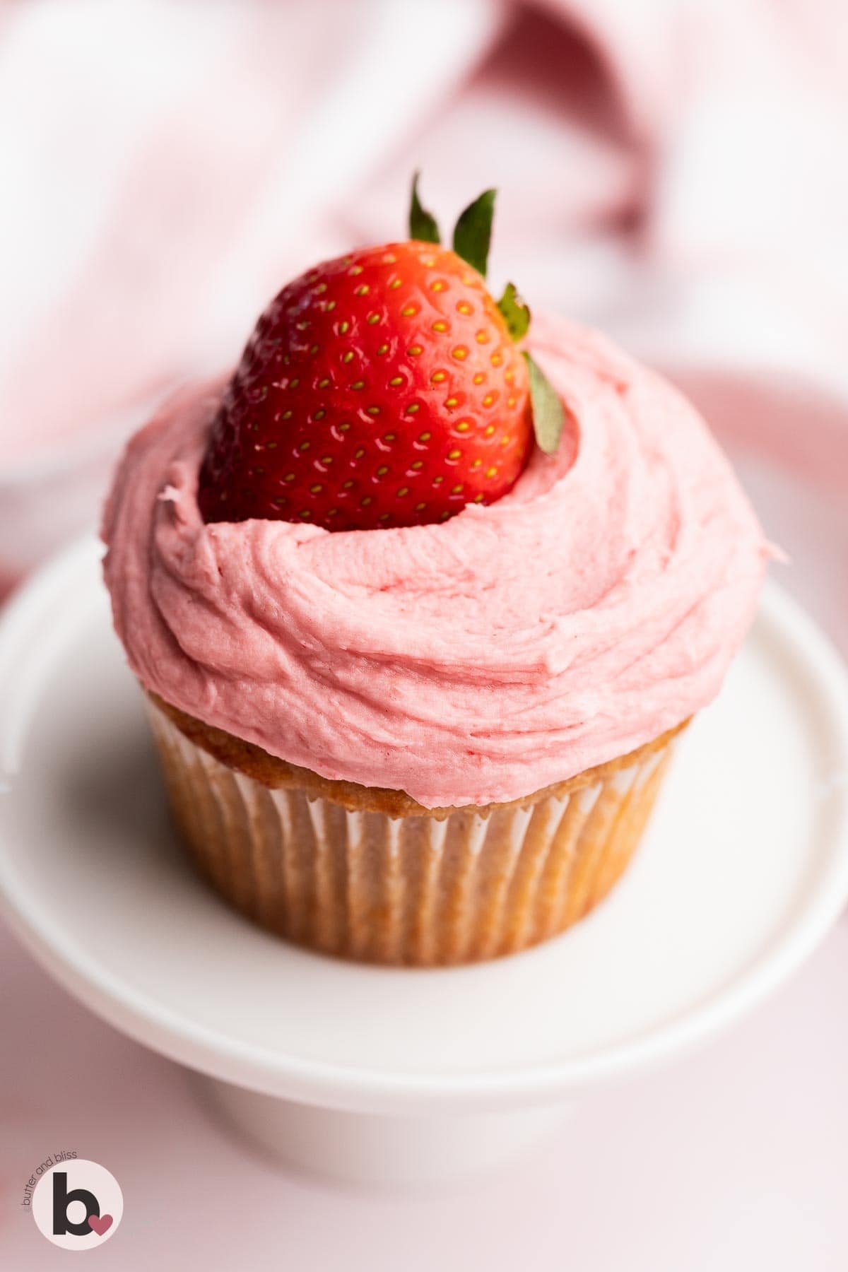 Cupcake with strawberry frosting topped with fresh strawberry.