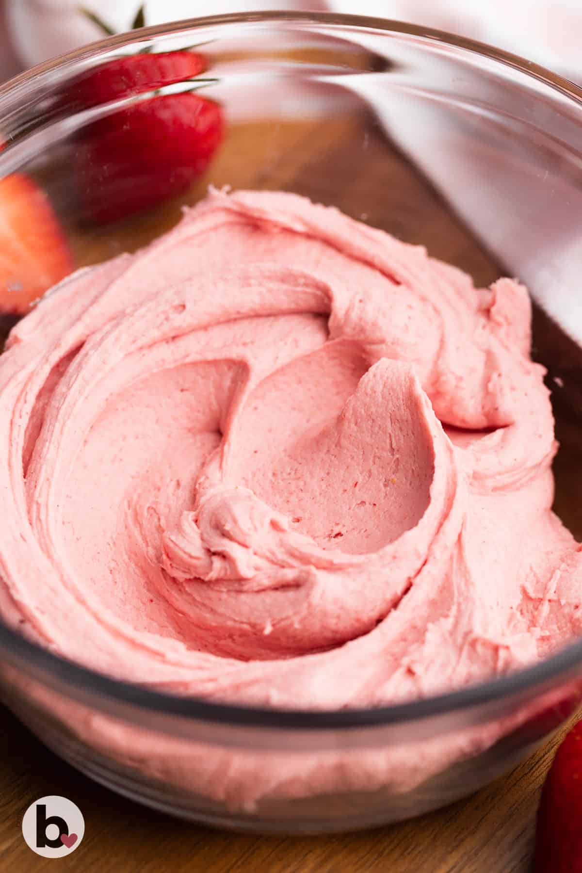 A bowl of strawberry frosting on a wood tray.