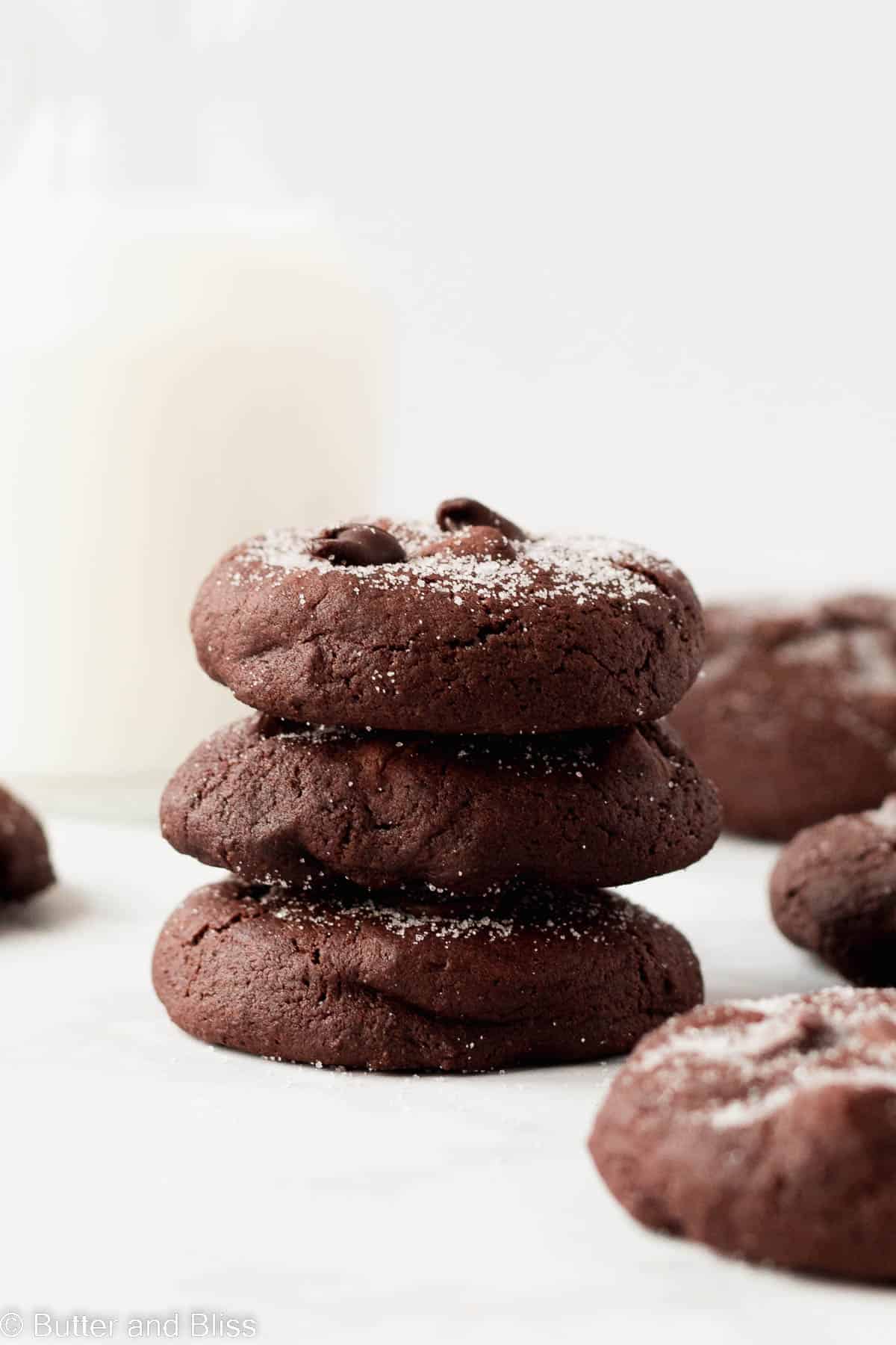 A small stack of double chocolate cookies set on a table next to a glass of milk.