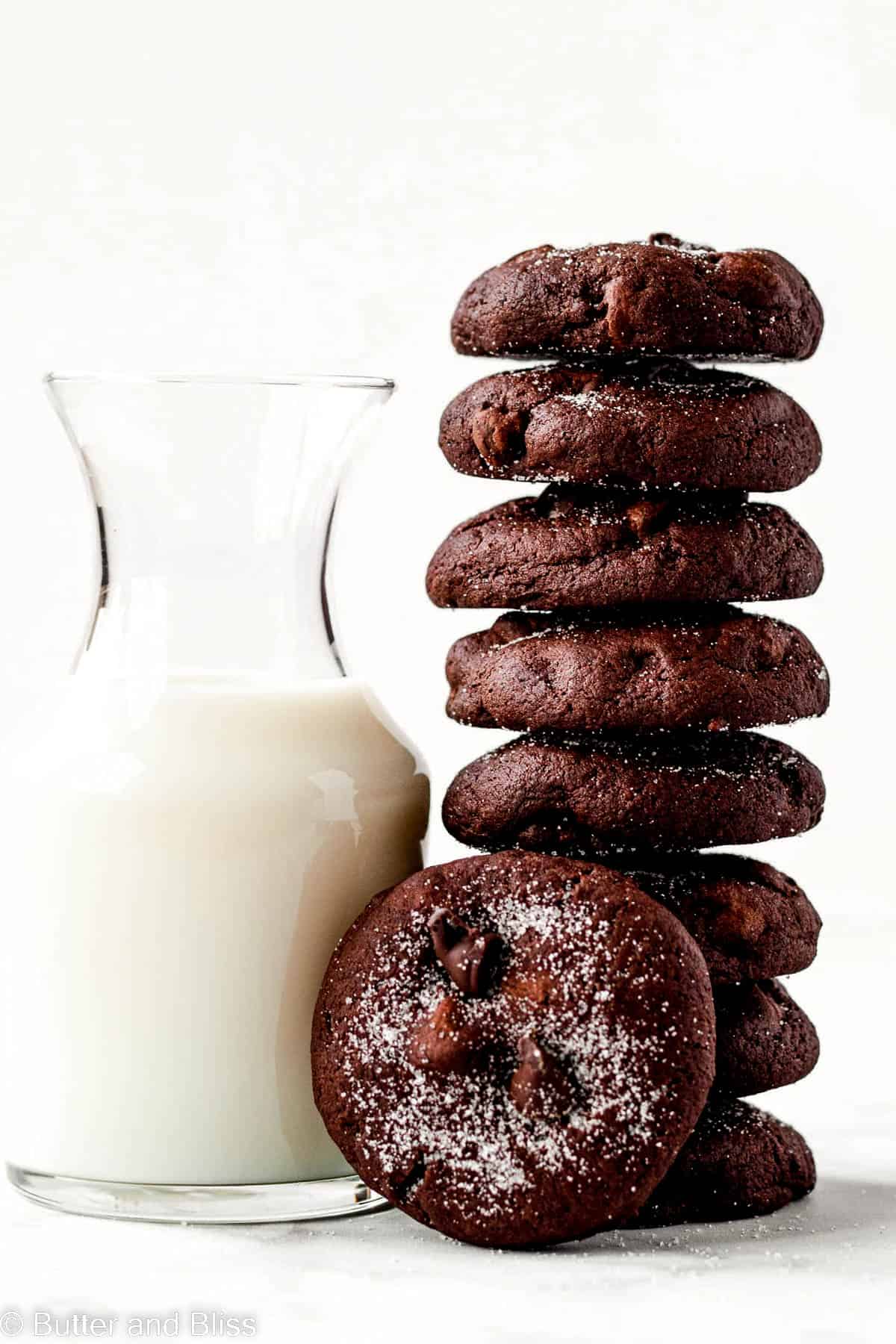 Tall stack of double chocolate chip cookies leaning against a glass of milk.