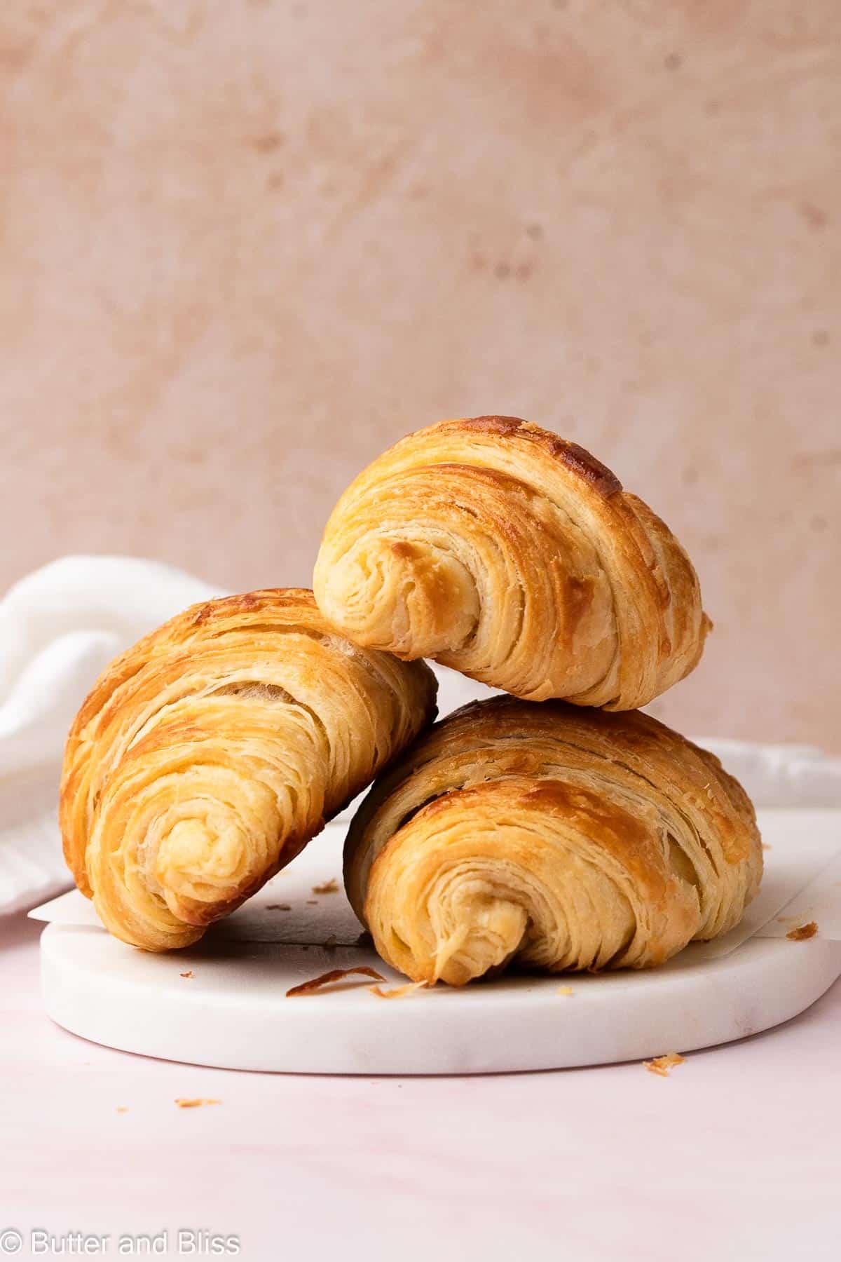 Three flaky croissants with tons of layers stacked on a white plate.