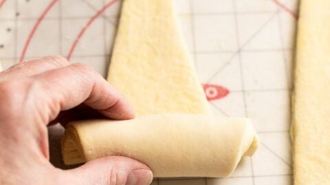 Hand rolling croissant dough triangle into crescent shape.