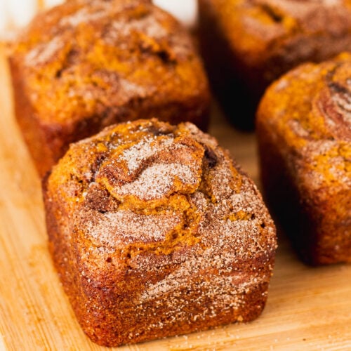 Pretty individual loaves of pumpkin bread on a wood plate with cinnamon swirl crunch topping.