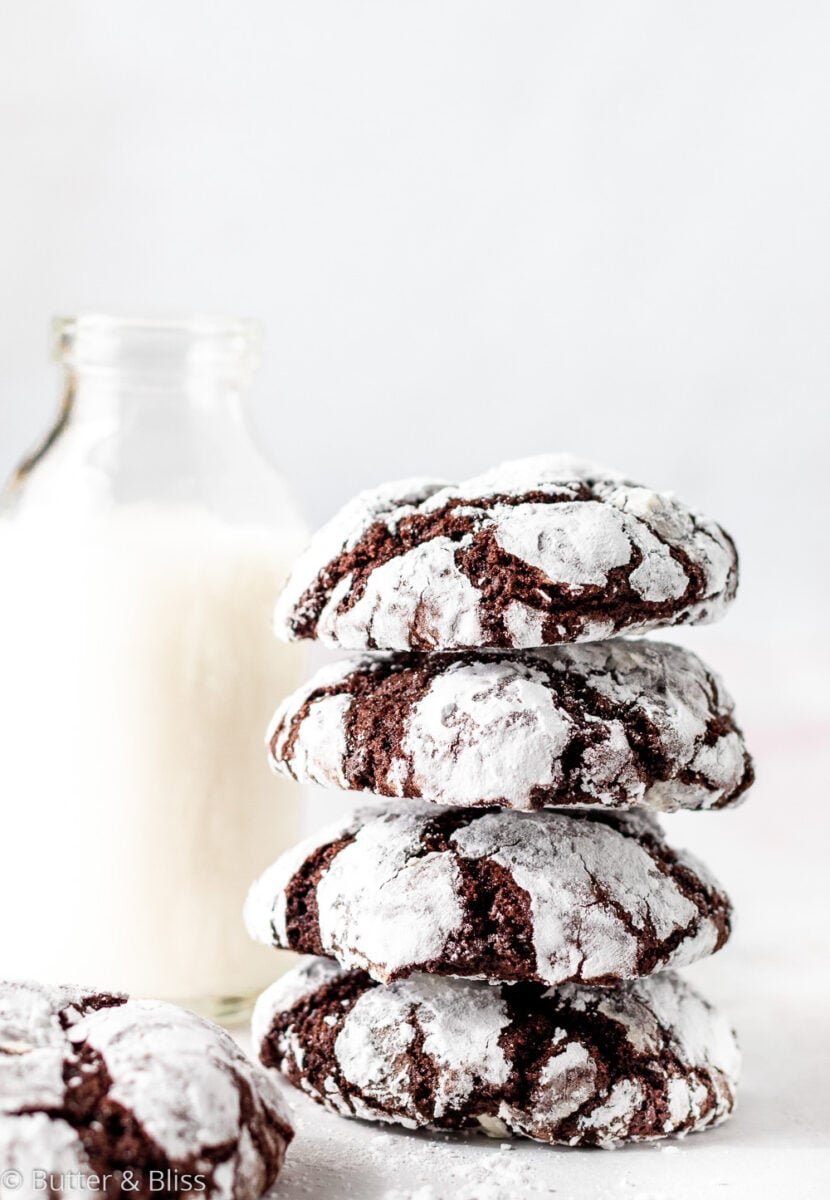 A stack of holiday cookies with powdered sugar coating next to a glass of milk.