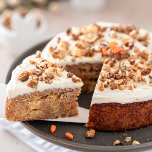 Frosted carrot cake with a slice cut on a platter