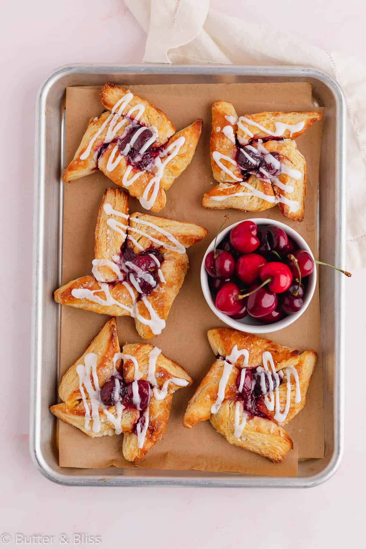 A baking tray of glazed pinwheel danish with cherry filling