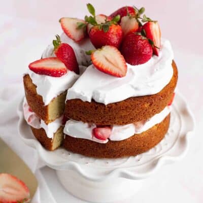 Pretty mini strawberry shortcake cake layered with whipped cream and fresh strawberries on a cake stand.