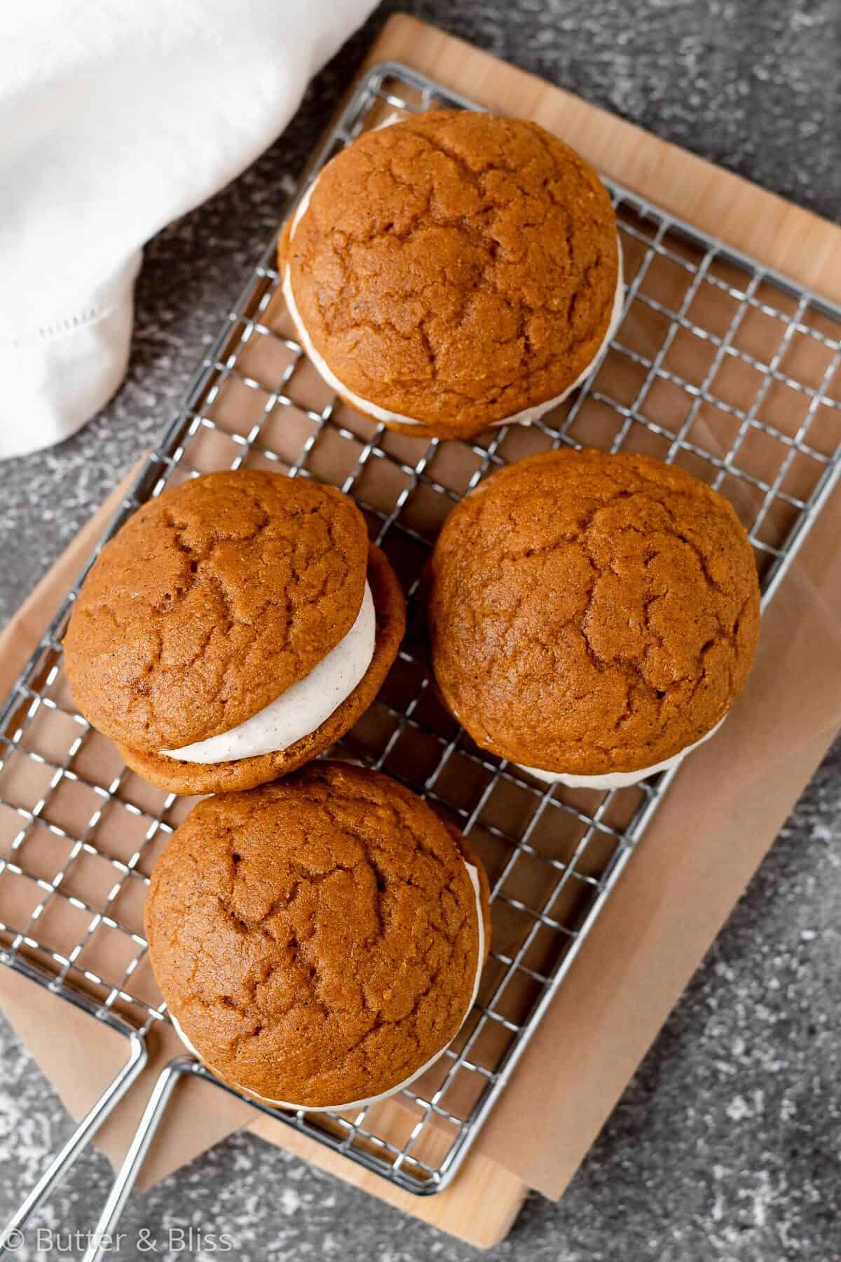 Pumpkin whoopie pies with cream cheese filling arranged on a wire rack