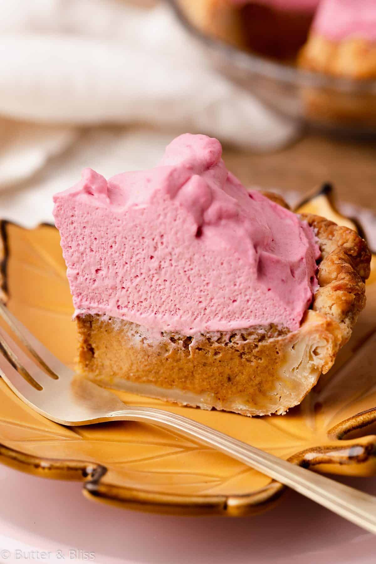 Slice of pumpkin pie with cranberry whipped cream on a small plate