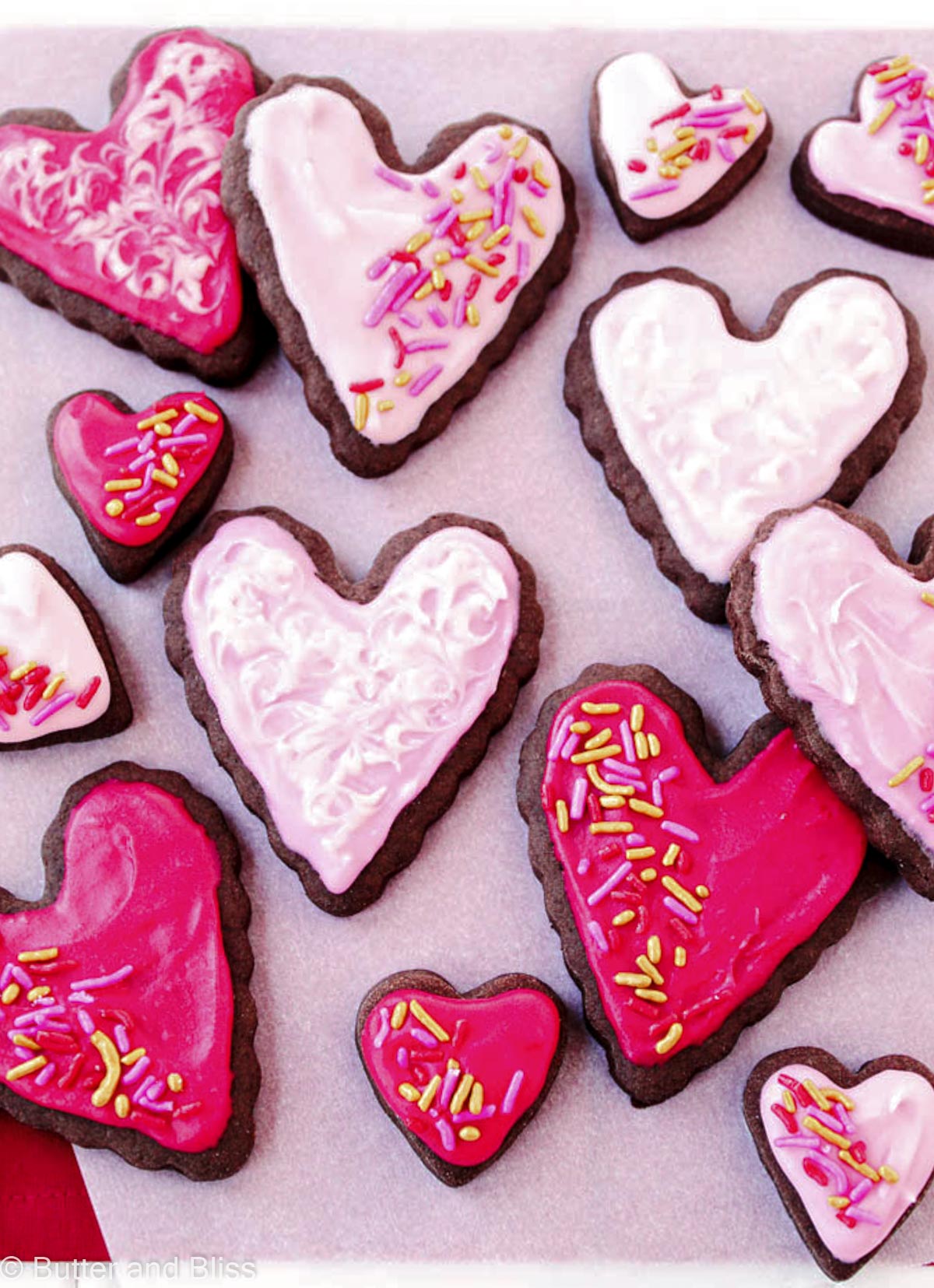 Chocolate sour cream sugar cookies cut in the shape of hearts and frosted on a piece of parchment paper.