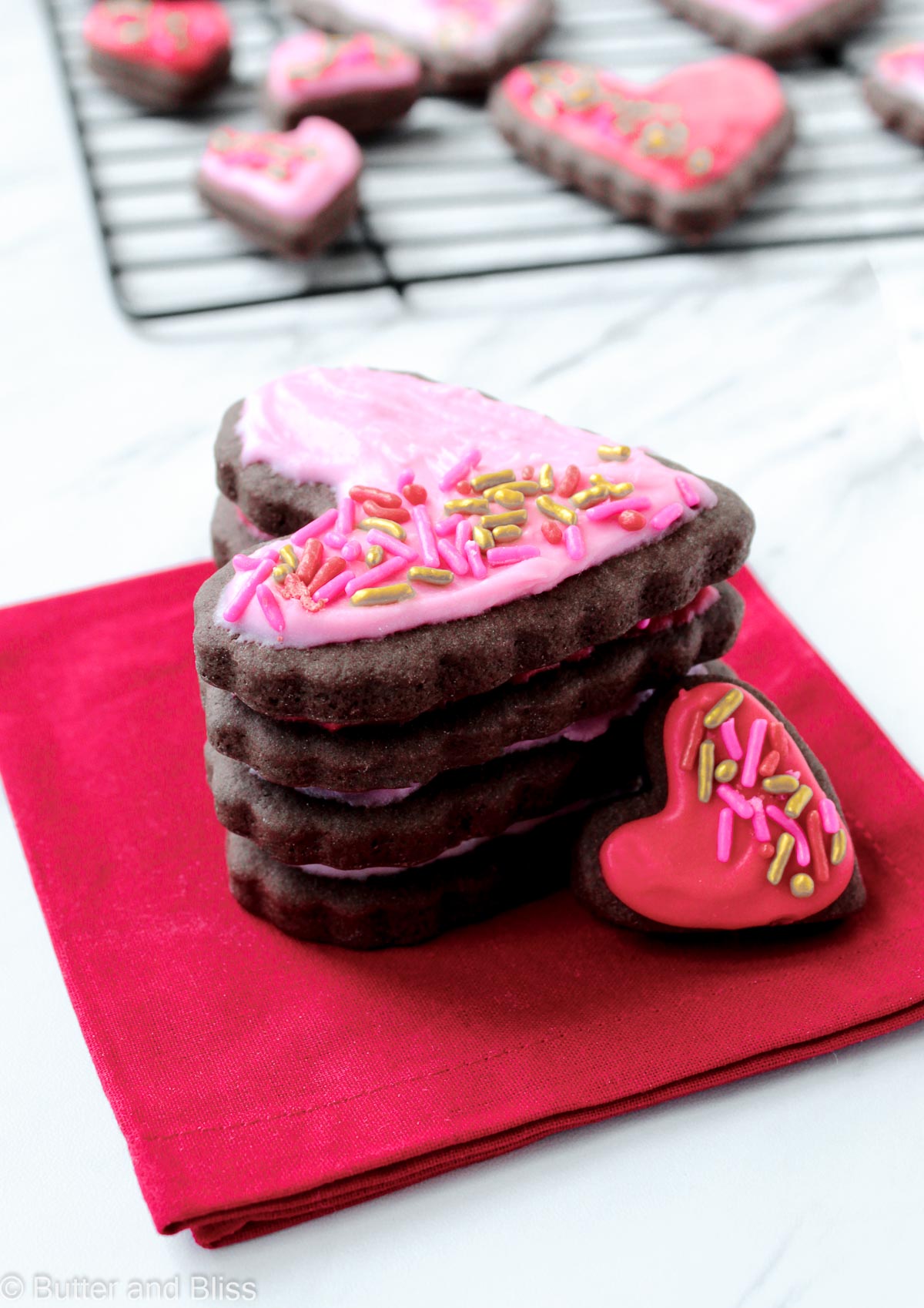 A stack of heart shaped chocolate sugar cookies frosted with Valentine's Day colored frosting and sprinkles.