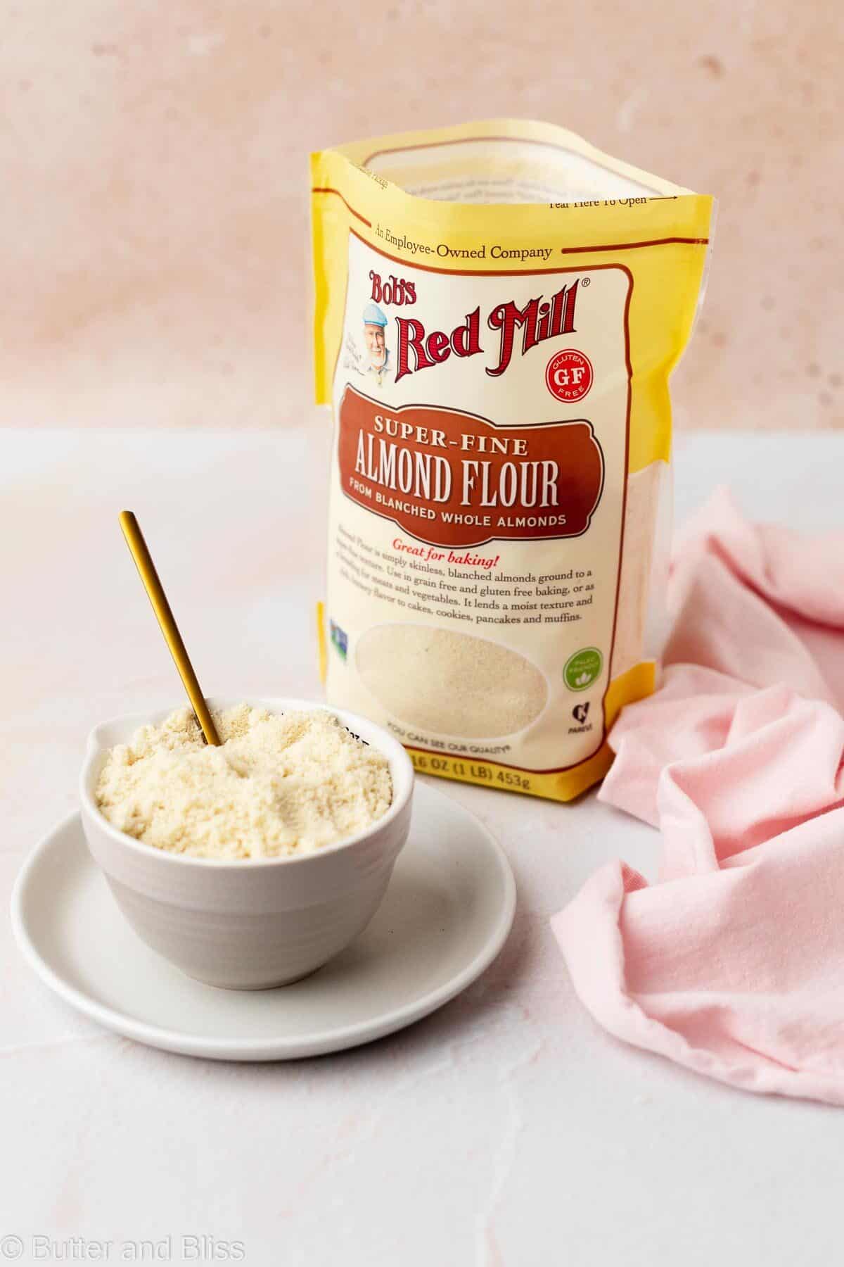 A bowl of almond flour next to a bag of almond flour.