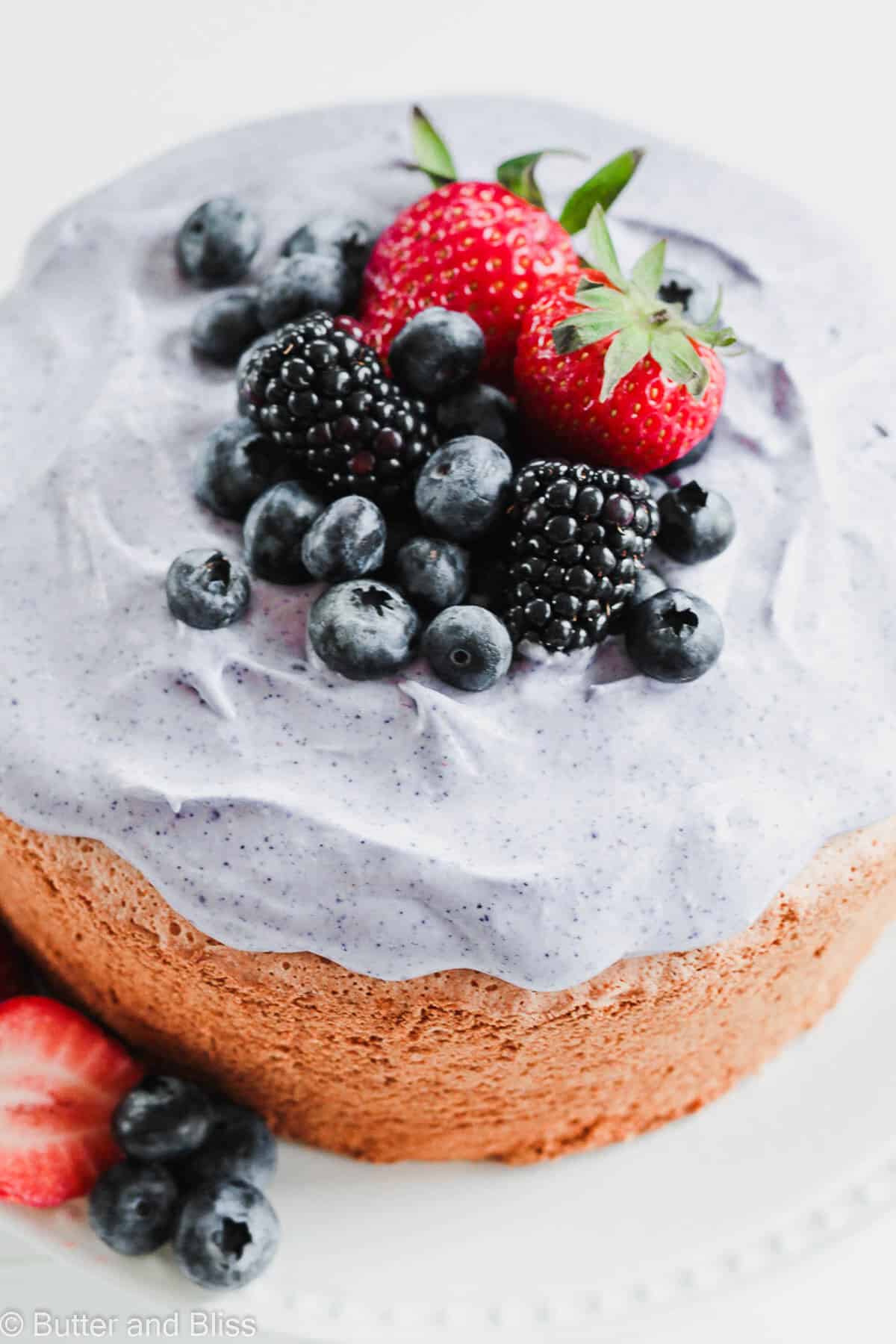 Close up of a mini angel food cake on a white plate with blueberry whipped cream