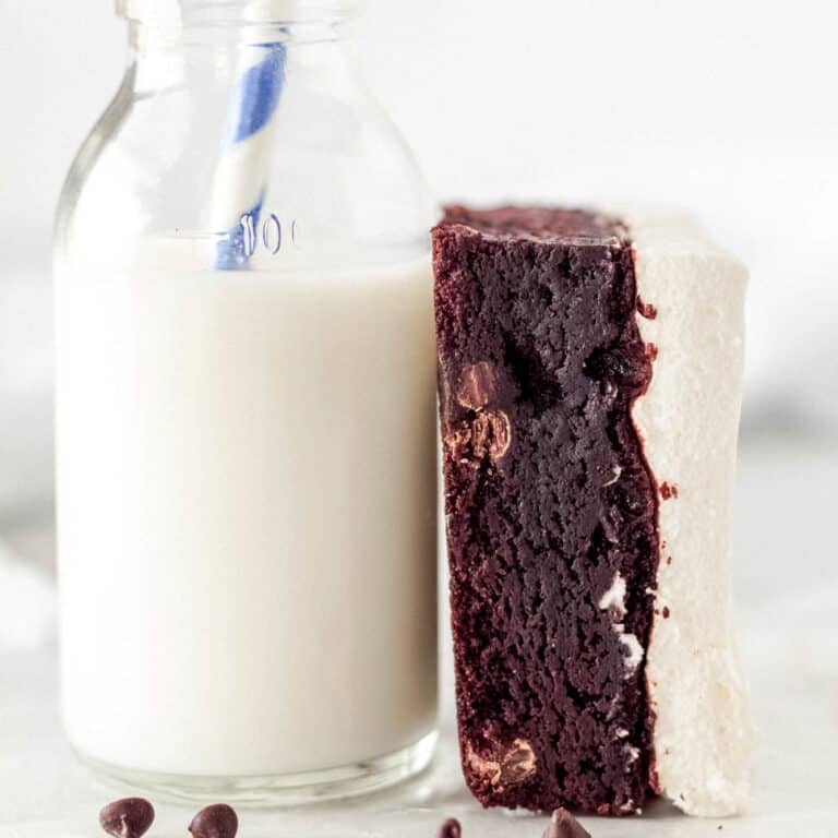 Fudgy brownie with whipped topping leaning against a glass of milk