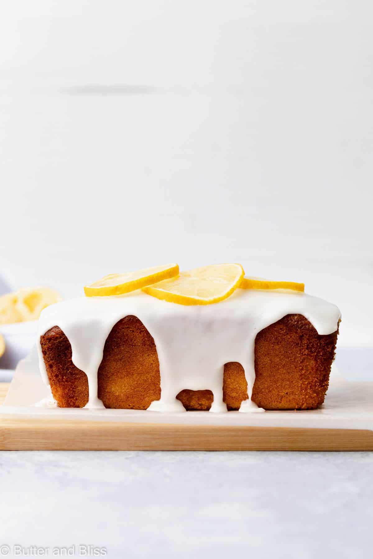 Side view of a mini iced gluten free lemon loaf on a wood cutting board