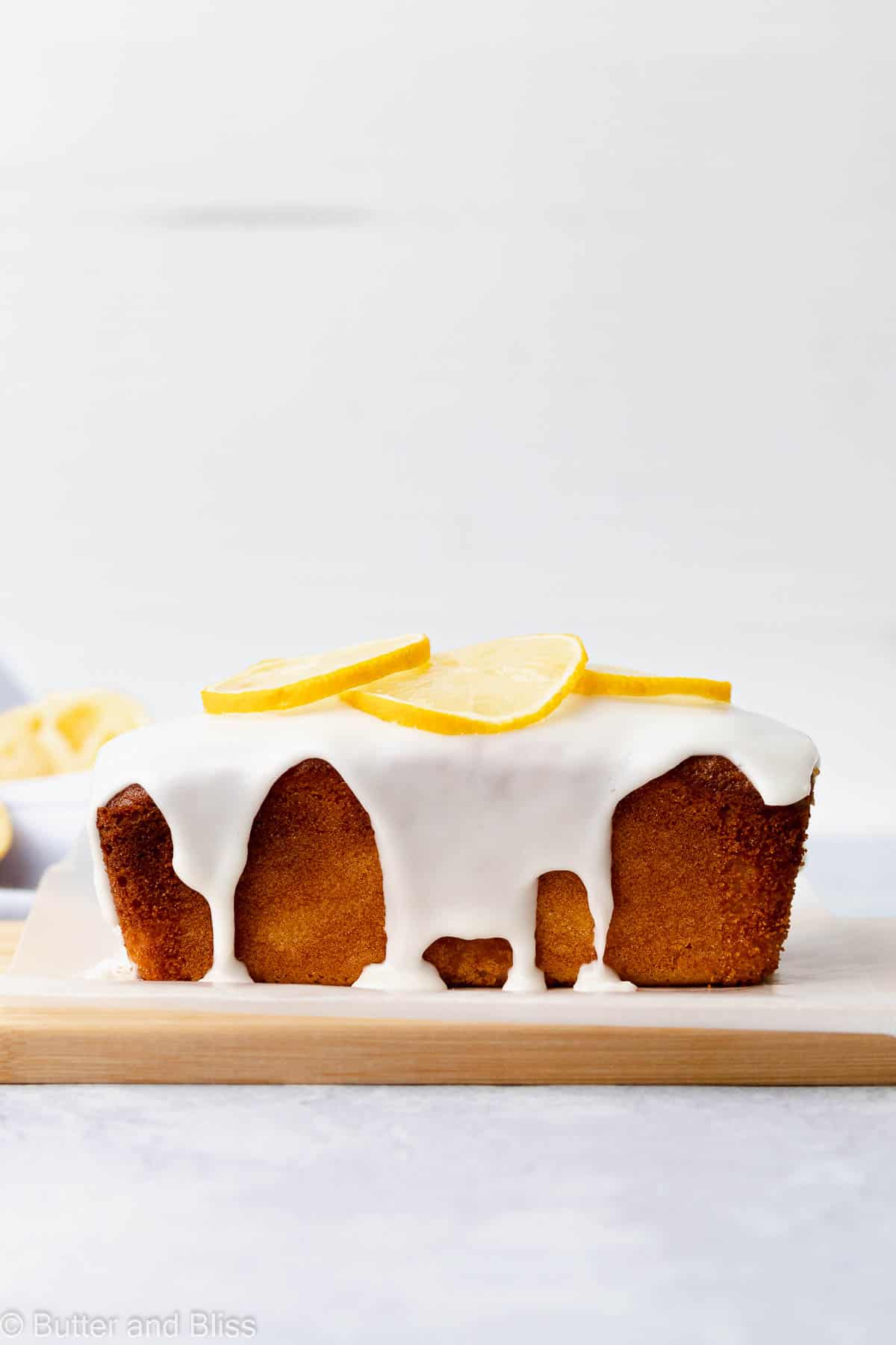 Side view of a mini iced gluten free lemon loaf on a wood cutting board for a delicious spring dessert recipe