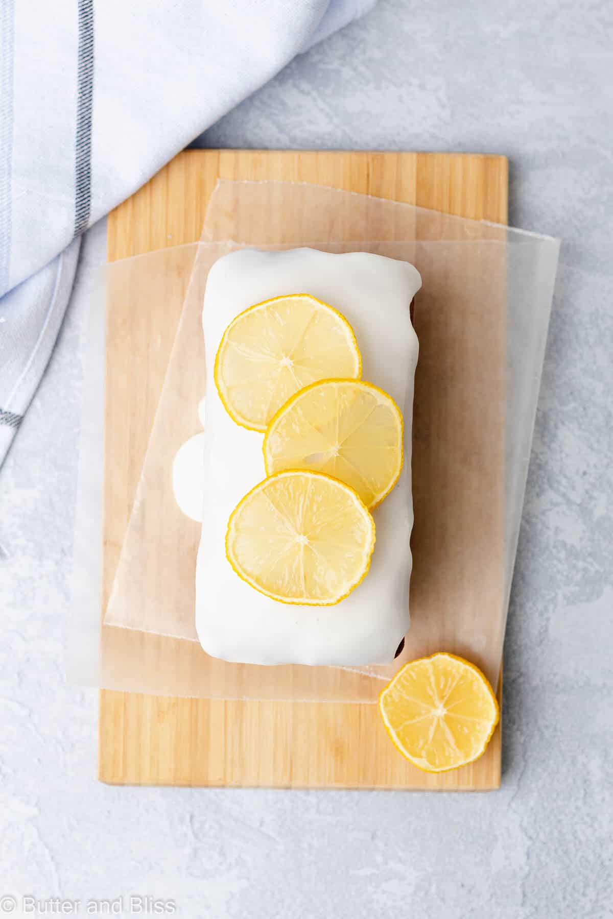 Gluten free mini lemon loaf with lemon slices and icing on a cutting board