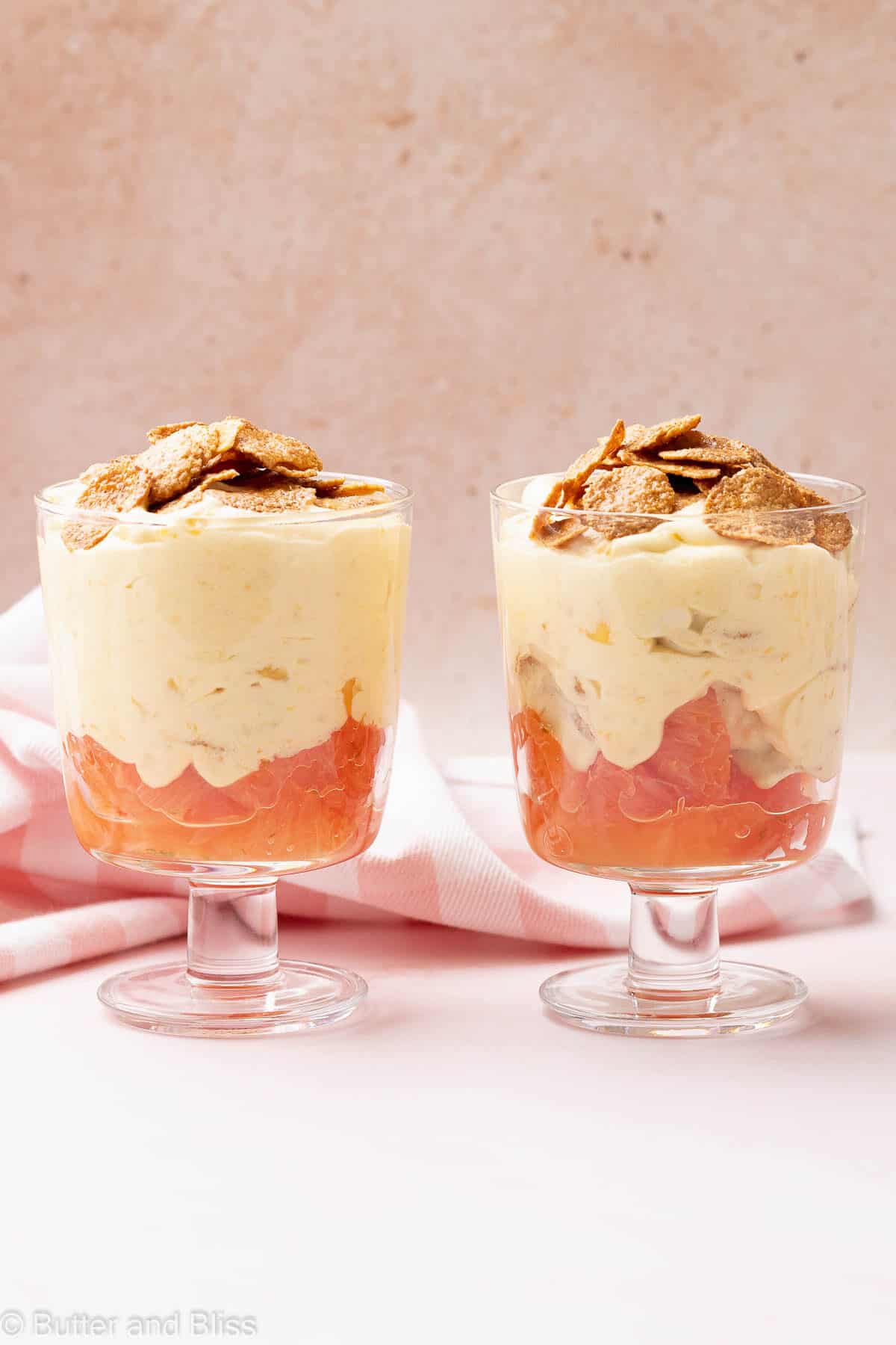 Two parfait glasses filled with mango grapefruit dessert lined up on a table