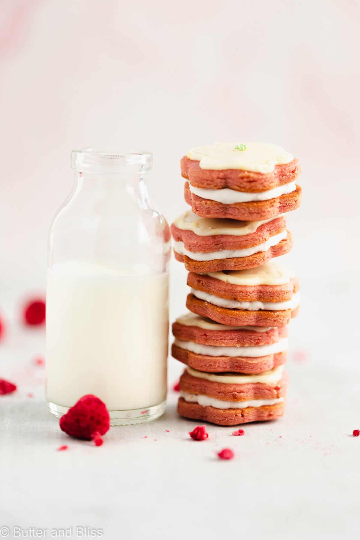 Stack of raspberry and lemon cookie sandwiches leaning against a glass of milk