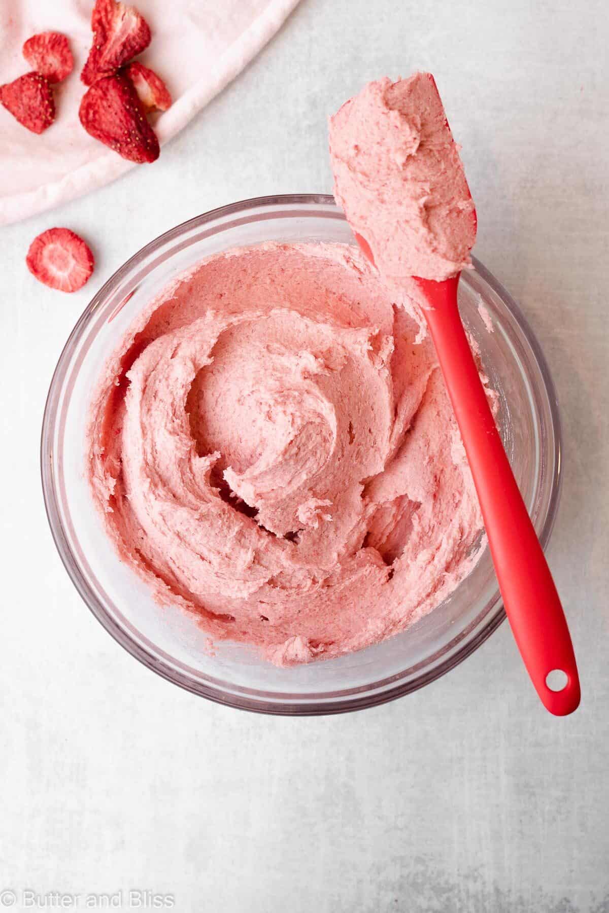 Top view of butter free strawberry frosting in a bowl with a red spatula