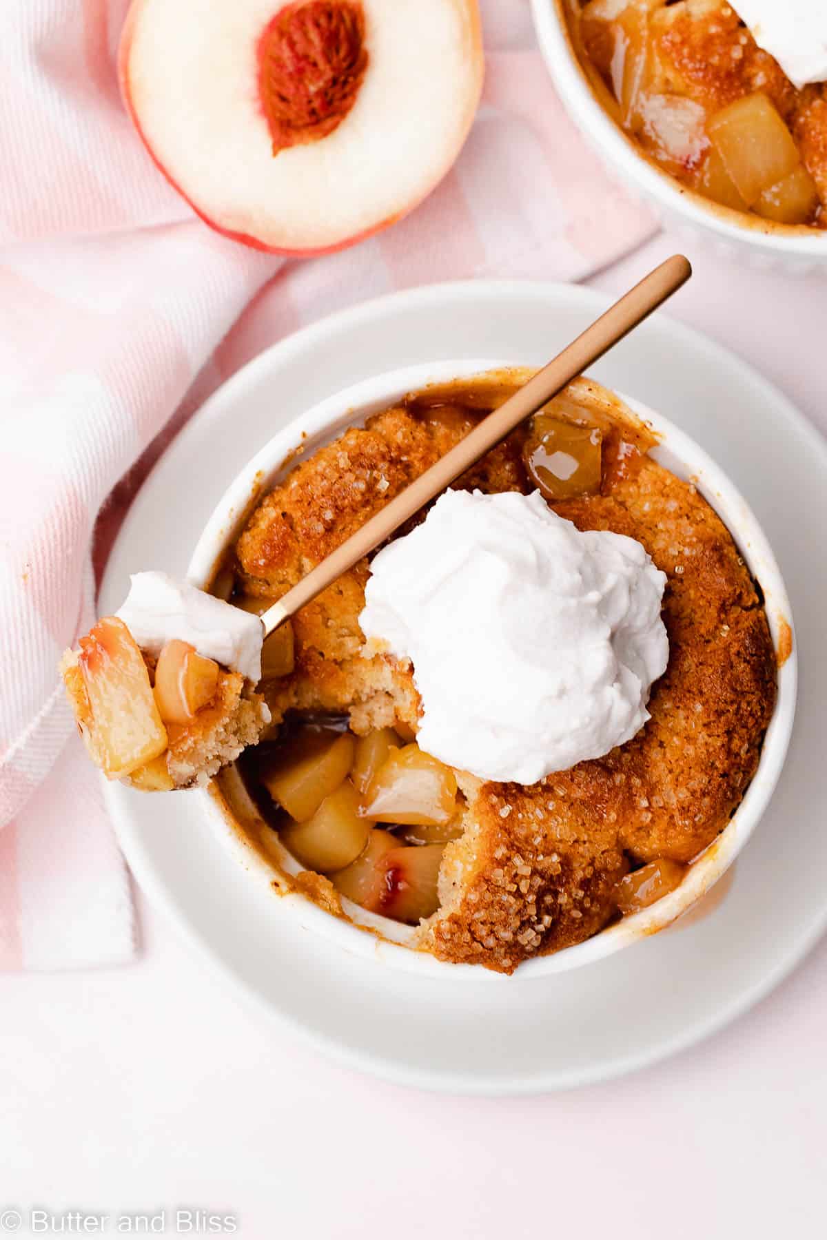 Top view of end of summer juicy peach cobbler topped with whipped cream on a spoon