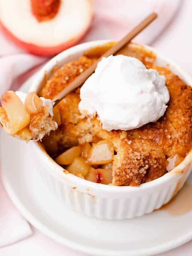 Close up of the inside of a juicy peach cobbler topped with whipped cream