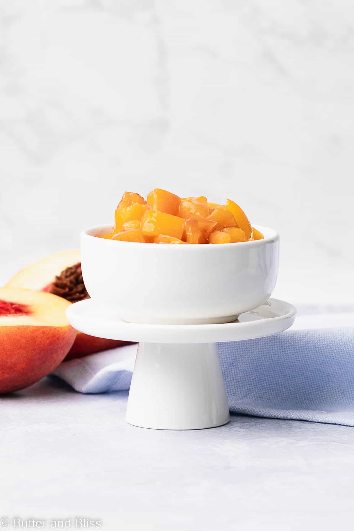 Peach compote in a small white bowl set on a mini cupcake stand