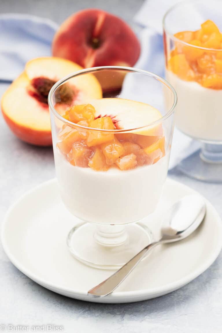 Peach panna cotta topped with peach slices in a parfait glass set on a white plate