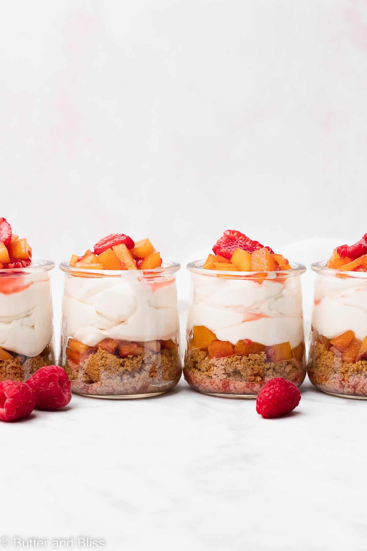 Four raspberry peach gluten free cheesecake cups in a row on a table
