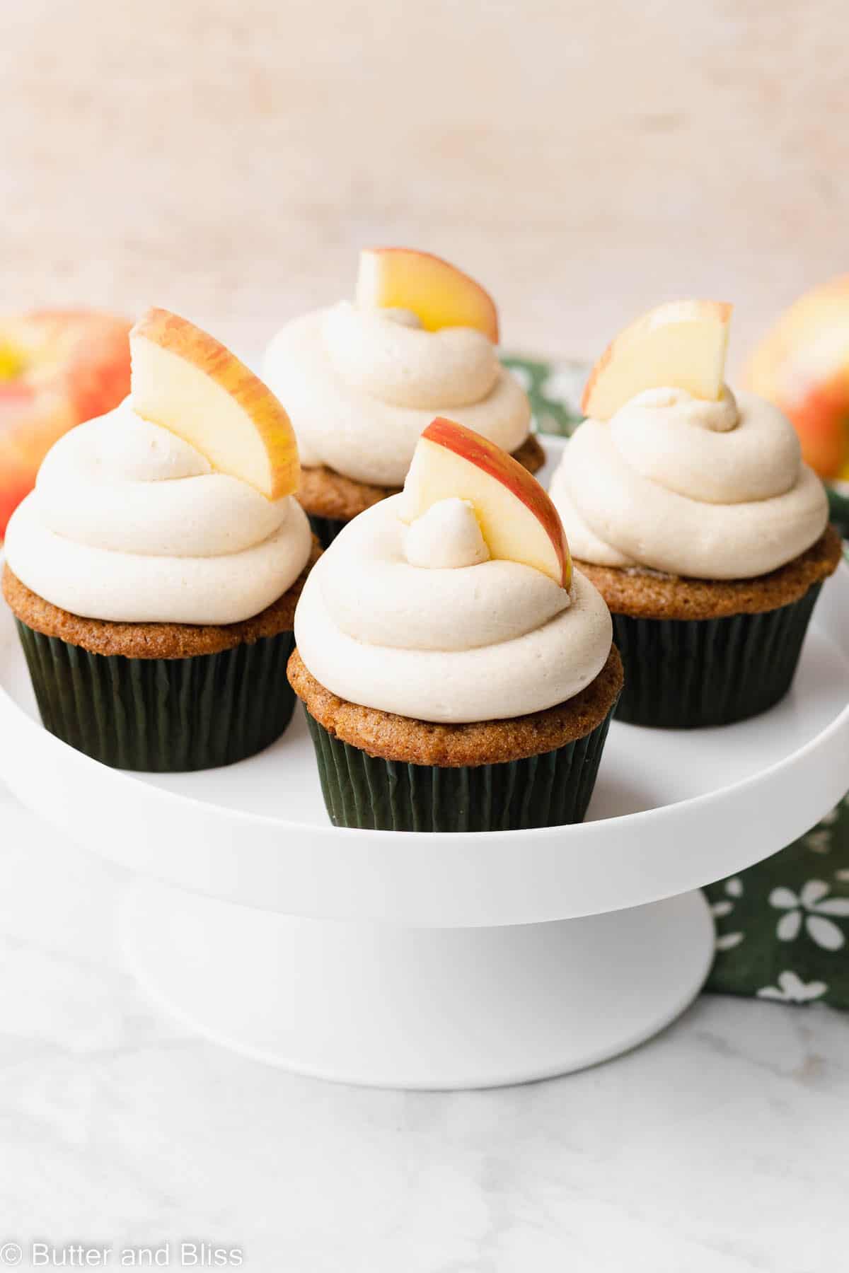 A cake platter of frosted gluten free apple spice cupcakes on a table.