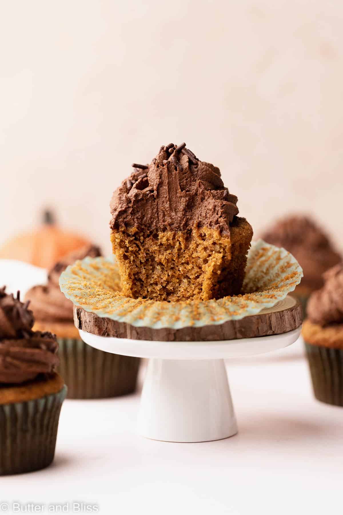 A gluten free pumpkin cupcake with chocolate frosting cut in half and placed on a small cupcake stand.