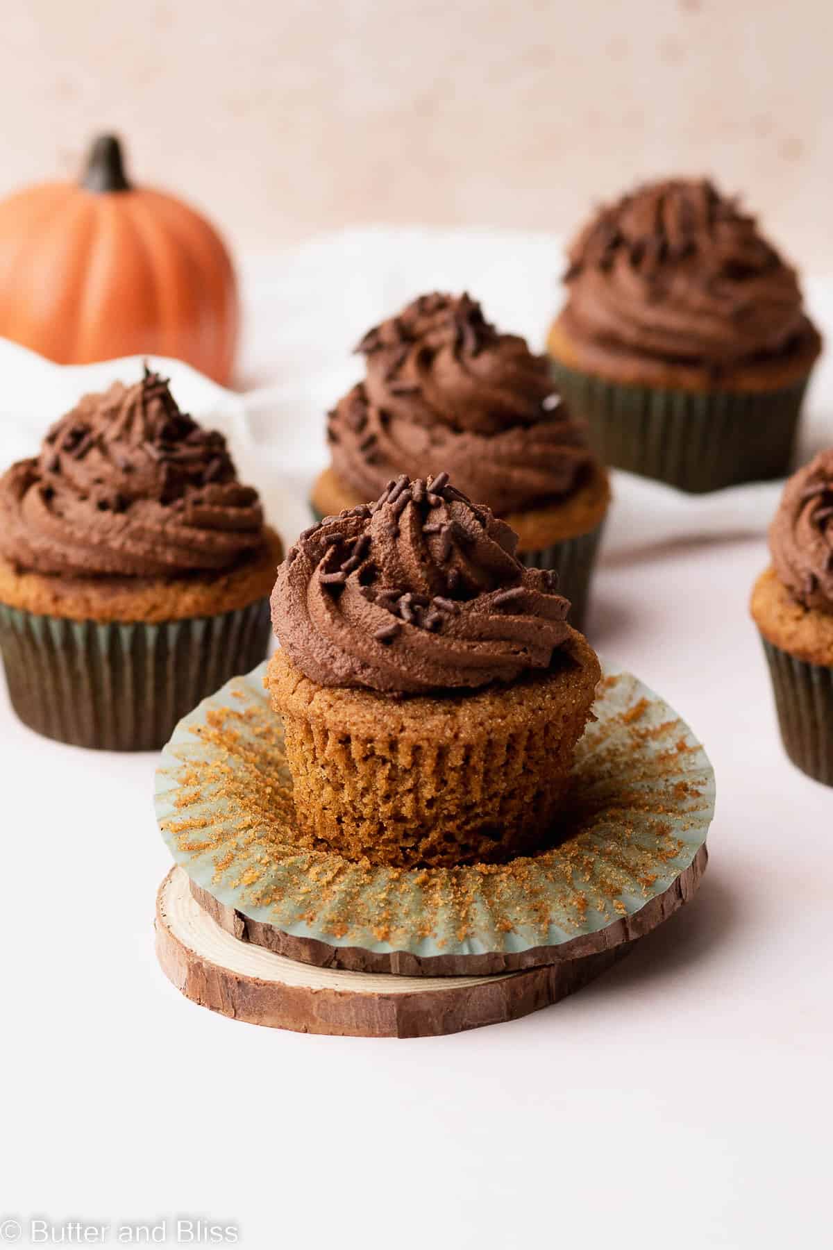 A frosted gluten free pumpkin cupcake set on a wooden plate with the cupcake liner removed.