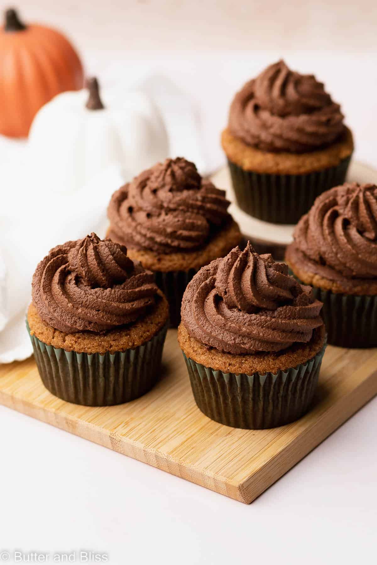 Whipped chocolate ganache frosting on pumpkin cupcakes set on a wood tray.