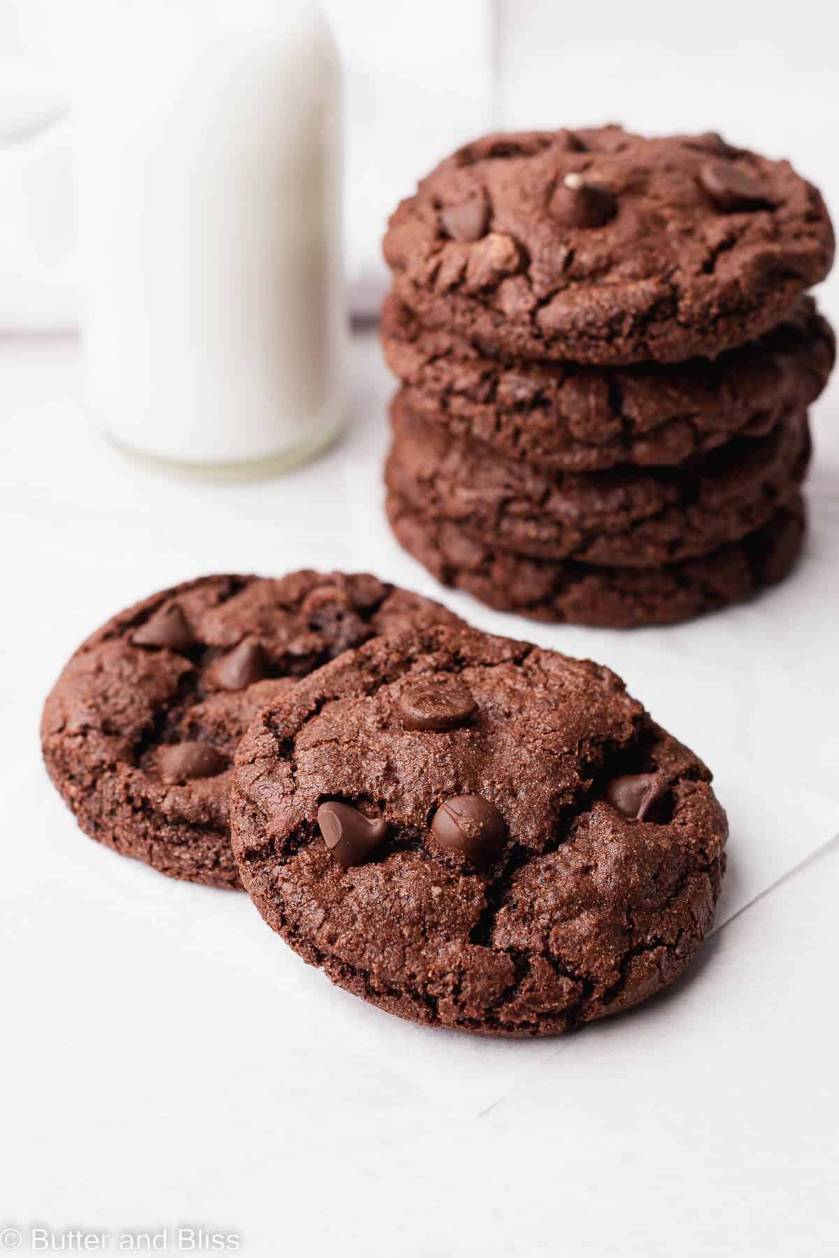 Two gluten free chocolate cookies stacked next to a glass of milk.