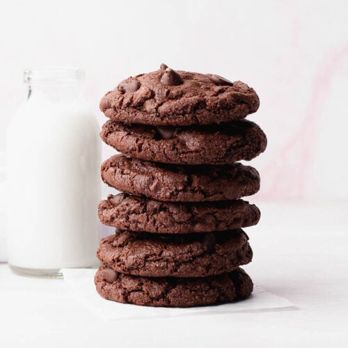A stack of small batch and gluten free double chocolate cookies next to a glass of milk.