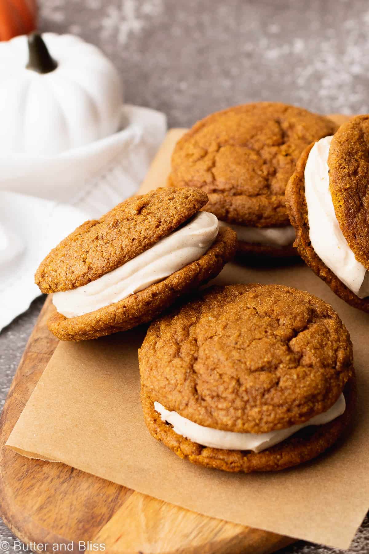 Filled pumpkin whoopie pies arranged on a wood cutting board.