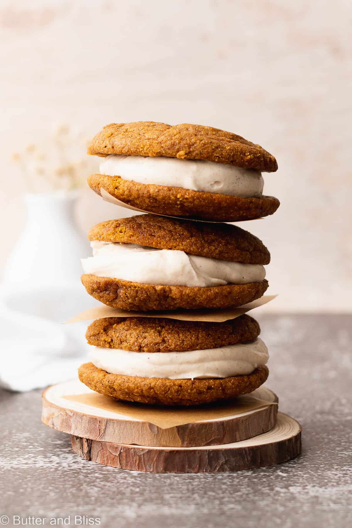 A stack of three pumpkin spice whoopie pies on a small wooden plate.
