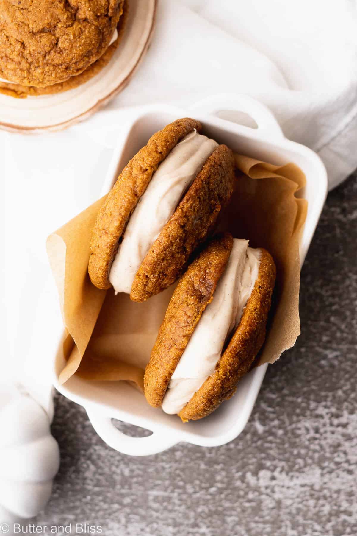 Gluten free pumpkin spice whoopie pies arranged in a pair in a small white dish.