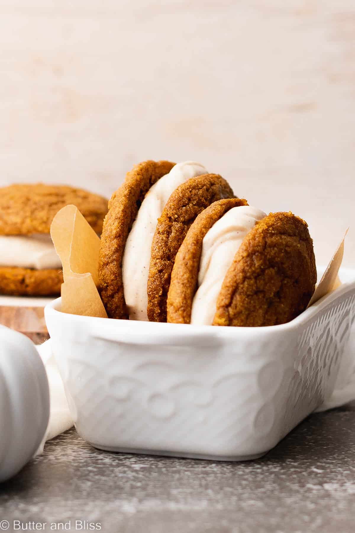 Two gluten free pumpkin spice whoopie pies set in a pretty white baking dish.