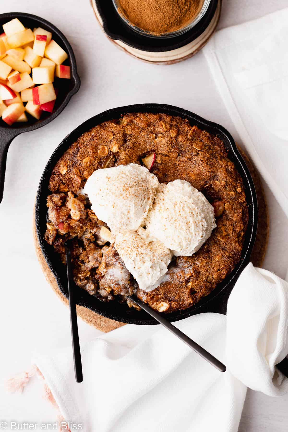 Top of an oatmeal caramel apple skillet cookie with ice cream and small spoons taking bites.