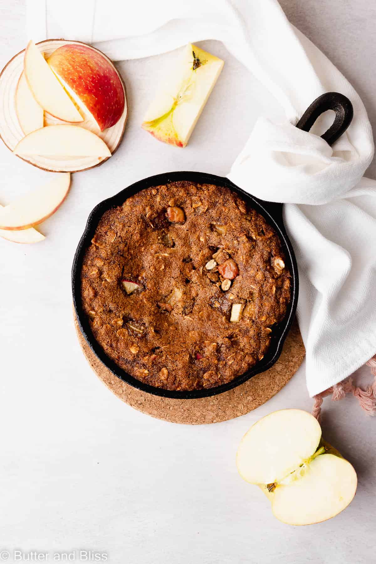 Freshly baked caramel apple oatmeal skillet cookie in a cast iron skillet on a wood tray.